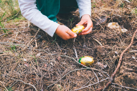 A girl's hand picks up a chocolate easter egg found in a forest.