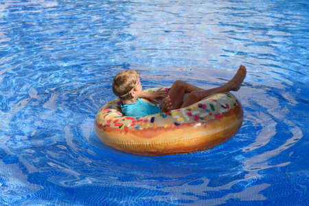 6-year-old boy bathing in a transparent pool playing with a large donut-shaped float.