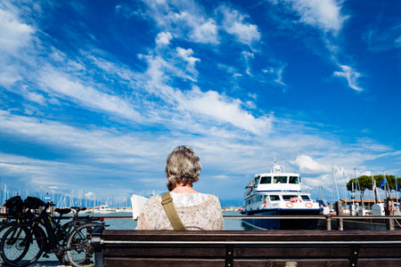 Verona, italy - september 21, 2021: A retired woman relaxes by reading a book sitting on a bench next to the promenade on a sunny day.のeditorial素材