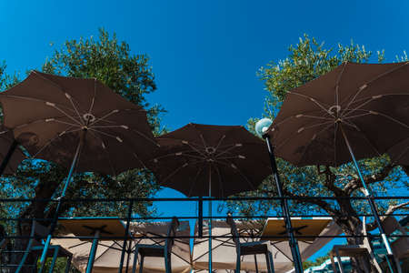 Open umbrellas to protect tourists who rest at tables on a terrace from the sun.の写真素材