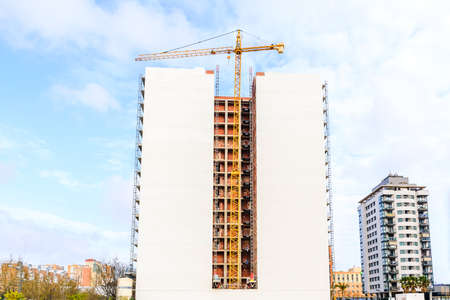 A building under construction with a smooth facade in a new area of the city, with a crane.