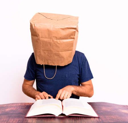 Funny man with his head covered with a paper bag reading and studying a book.の写真素材
