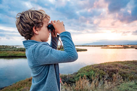 An adventurous boy explores the landscape with binoculars with the cloudy horizon, concept of growing up with independence and future.の写真素材