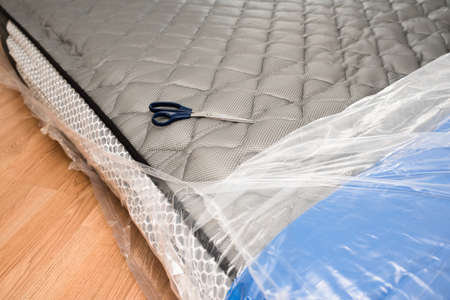 Unwrapping new mattress from its plastic wrap with scissors, it expands quickly.の写真素材