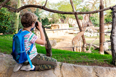 Valencia, Spain - December 28, 2021: A young boy observes a captive giraffe using binoculars in a zoo.のeditorial素材