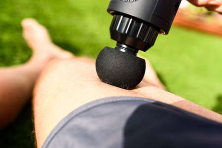 Assistant massages the legs of an athlete with a percussion massage gun to recover from an intense...