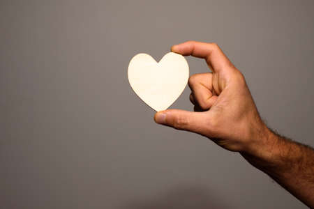 Man's hand holds an empty wooden heart isolated on a gray background.