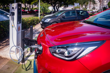 Valencia, Spain - July 6, 2021: Red car recharging its lithium electric batteries at a free public...