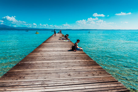 Desenzano del Garda, Italy - September 22, 2021: Tourists enjoy the sun on the shores of Lake Garda on a wooden walkway.のeditorial素材