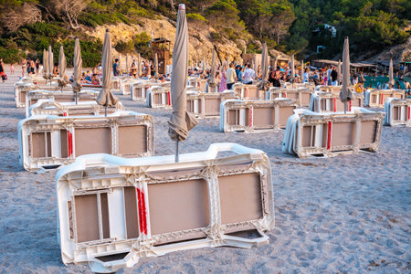 Ibiza, spain - july 25, 2022: Plastic sunbeds on a beach, folded at sunset, next to tourists and vacationers.のeditorial素材