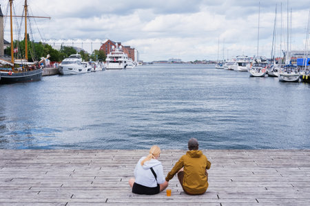 Copenhagen, Denmark - August 8, 2023: A couple relax on a pier, watching the docked boats.のeditorial素材