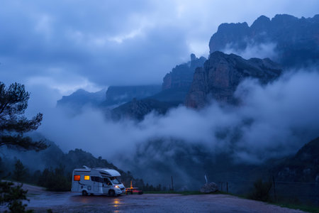 A camper is parked in the middle of a road with mountains in the background.の素材