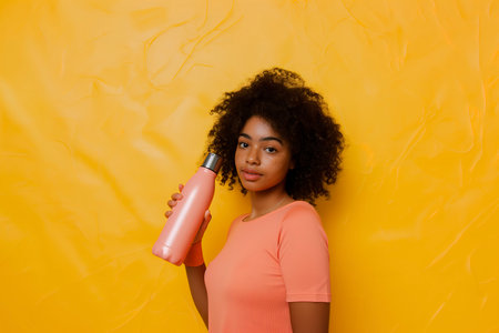 Young woman using a hair dryer in front of a vibrant yellow wall.の素材