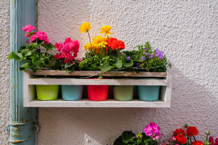 A window box overflowing with various potted plants is positioned next to a brick wall. The plants display vibrant colors and different textures in this urban setting.の写真素材