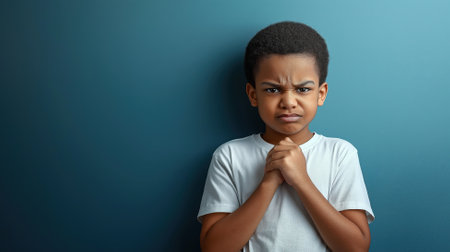 An angry dark-skinned boy in a white t-shirt stands with folded hands, showing vivid expressions against a blue backdrop.の素材