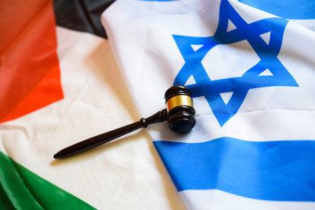 Israeli and Palestinian flags lie together with a gavel, symbolizing the pursuit of international...