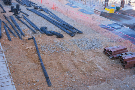 At a construction site, steel rebar and various tools are scattered along with gravel. Workers...