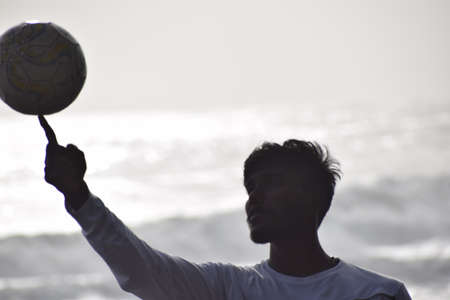 Silhouette of a man holding a soccer ball on the beachの写真素材