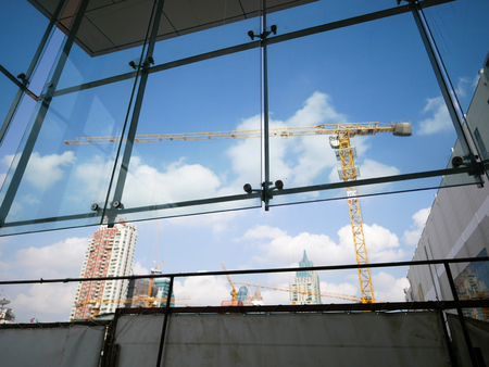 Construction crane through glass window with background of blue sky.の写真素材