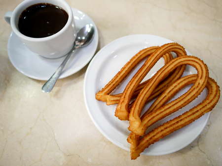 Churros or Spanish fried-dough pastry on white plate served with a cup of hot chocolate as dipping sauce.の写真素材