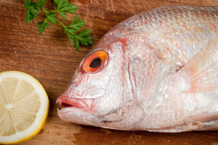 Fish (dorade, gilthead, sparus aurata) with lemon and parsley on a wooden boardの写真素材