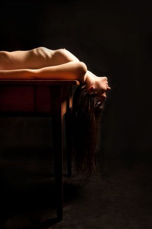 Classical nude of a beautiful young woman lying on a wooden table  の写真素材