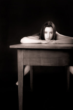 Portrait of a beautiful nude woman bending over an old wooden table, monochrome の写真素材