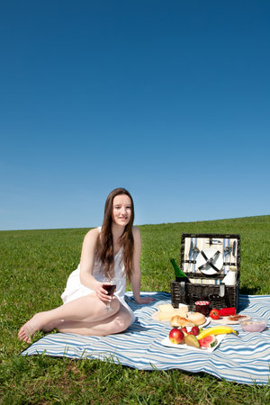 Beautiful young woman having a picnic on a green meadow under blue skyの写真素材