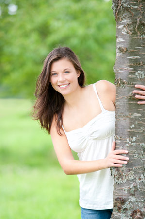 Outdoor portrait of a cute teen behind a tree in summerの写真素材