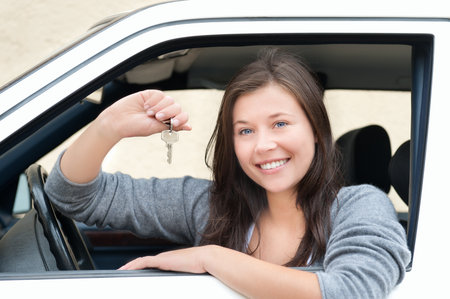 Young woman sitting in car and showing key. She is happy about her new drivers license or new carの写真素材