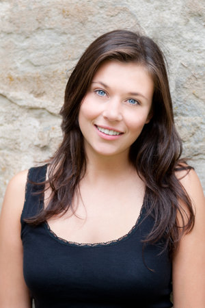 Closeup portrait of a beautiful smiling teen in black top in front of ancient wallの写真素材