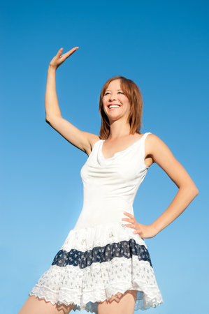 Outdoor fashion portrait of waving young woman with in white summer dress under  deep blue skyの写真素材
