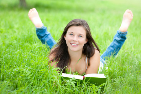 Outdoor portrait of a cute teen reading a book while lying in green grass の写真素材