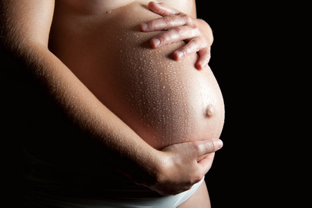 Wet belly of a beautiful pregnant woman in front of black backgroundの写真素材