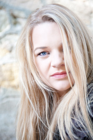 Closeup outdoor portrait of a beautiful young blond woman in front of an old wall