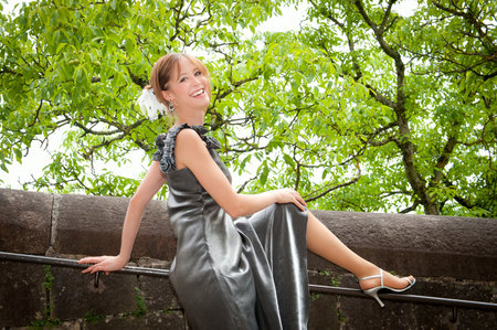 Outdoor portrait of a beautiful young woman in silver dress and high heels in front of ancient wallの写真素材