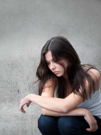 Outdoor portrait of a sad teenage girl looking thoughtful about troubles in front of a gray wall 