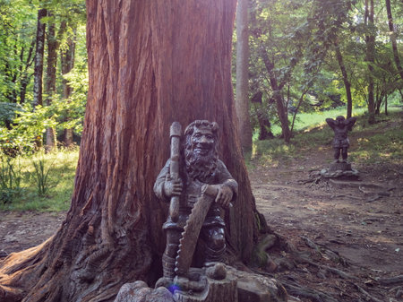OLYMPUS DIGITAL CAMERASculpture of a gnome with a saw by the tree. Park Arboretum. Russia Sochi 06 23 2019のeditorial素材
