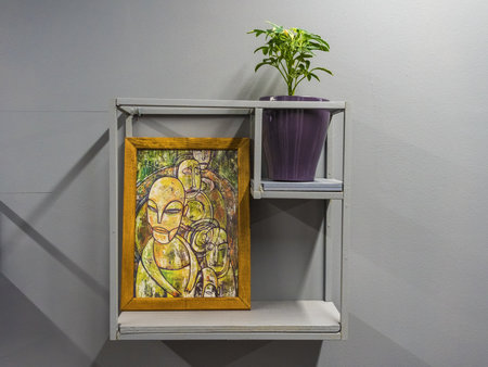A green plant in a purple pot with a picture next to it stands on an iron shelf nailed to wallのeditorial素材