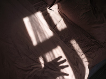 Beautiful shadow from the window and hand on bed from the morning sunの写真素材