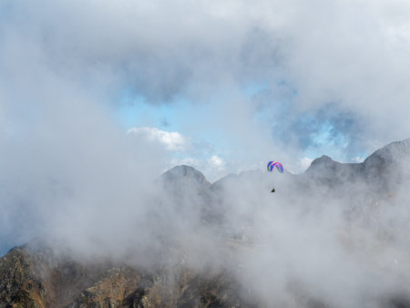 Paraglider flies over the mountains through cloudsの写真素材