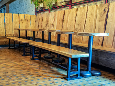 Wooden tables and benches with a metal base stand on a wooden floor along wooden low walls in an...