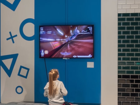 Sochi, Russia - 13 October 2019. Girl playing a game console looking at a screen hanging on a...
