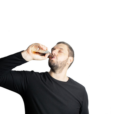 Dark-haired bearded man in dark clothes drinks a dark drink from a bottle closing his eyes in...