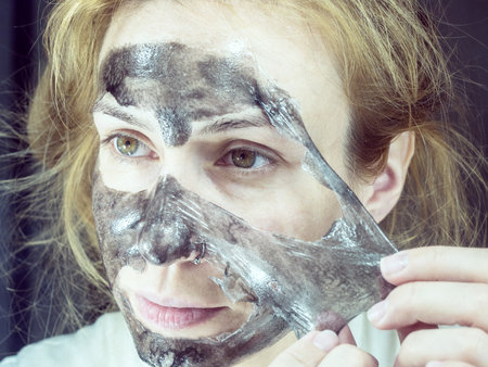 Close-up photo of a girl removing black thin mask from her faceの写真素材