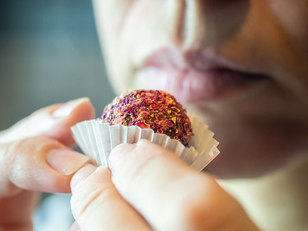 Round candy sprinkled with dry petals in a white wrapper on the background of female lips