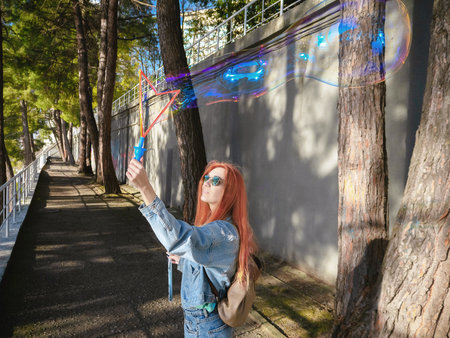 Girl inflates a beautiful soap bubble against the background of trees