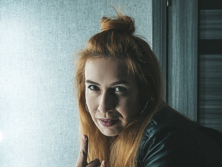 A girl in a black leather jacket shows a gesture of rock against a wall background with gray...