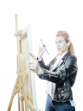 Beautiful girl artist stands in front of easel with a brush on a bright white background. High key styleの写真素材