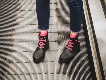 Female legs in blue jeans and black wet rubber boots with pink laces stand on the escalator